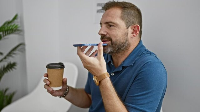 A middle-aged man with gray hair talks on the smartphone while holding a coffee cup in a modern interior setting.