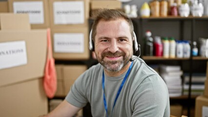 A smiling middle-aged man with a headset working indoors in a donation center warehouse.