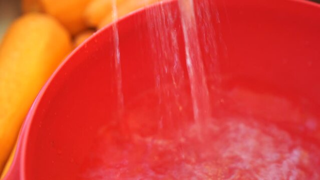 A red bowl with water pouring out of it. The bowl is filled with oranges.