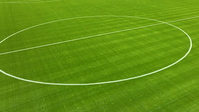 Aerial Close-up of a soccer field's central circle with freshly painted white boundary lines on vibrant green grass - panorama left to right
