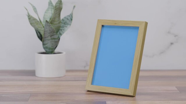 Wooden picture frame on countertop with replaceable blue screen on white background | 4K