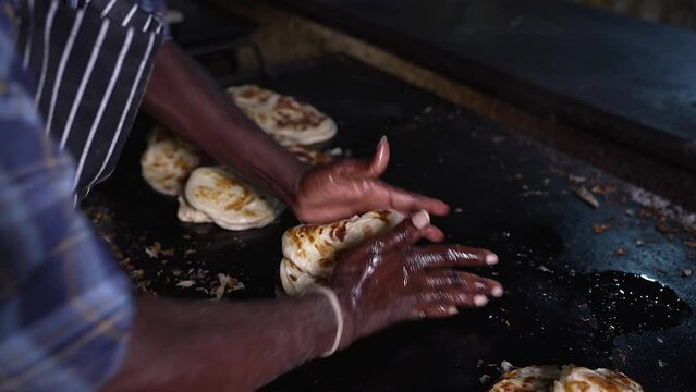 Close-up of a man's hand beating the hot parotta. Slow motion of crumpling the stack of hot parottas with both hands.