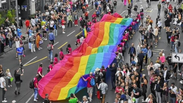 Many people wave huge rainbow flag. Big crowd walk city street. Fun lgbt community symbol. Stop no homophobia concept. Joy pride month fest. Bi gay men go csd love day party. Queer culture festival.