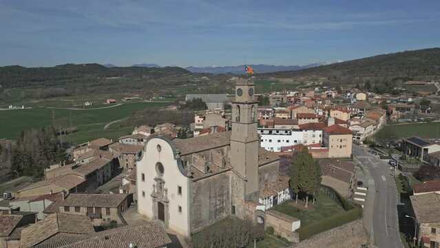 Orbital aerial drone view of a little catalan town with a clock tower with a pro-independence flag