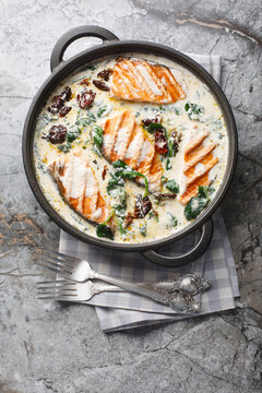 Tuscan grilled salmon in creamy sauce with spinach, sun dried tomatoes and parmesan closeup in the pan on the table. Vertical top view from above