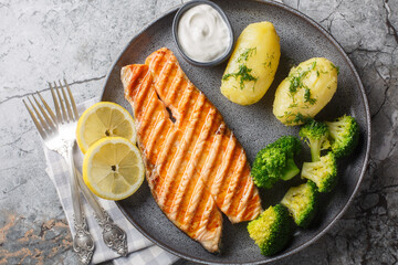 Delicious grilled salmon steak with boiled new potatoes, broccoli, lemon and cream sauce close-up...