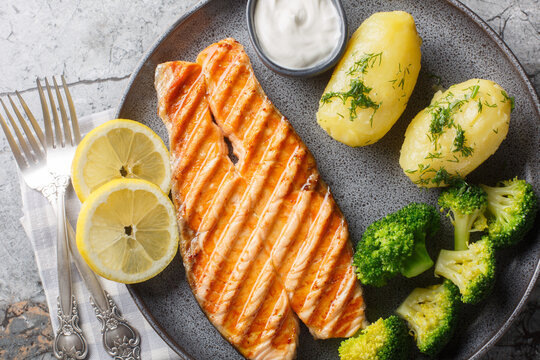 Grilled salmon, boiled potatoes, broccoli and cream sauce in a plate on the table. Horizontal top view from above