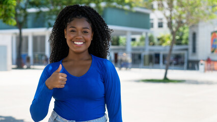 Pretty african american young adult woman showing thumb up with copy space in the city