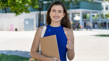 Successful young caucasian female student with brunette hair showing thumb up
