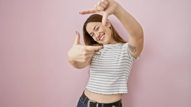 Young hispanic woman with blue eyes standing smiling making frame with hands and fingers with happy face. creativity and photography concept. over isolated pink background