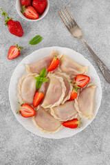 Tasty traditional dumplings, varenyky or pierogi with strawberry and sour cream on a white plate.