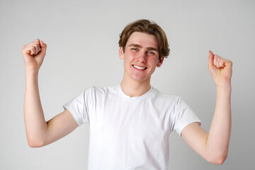 Young Man With a Joyful Expression Raising His Fists in Victory Against a Neutral Background