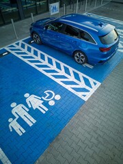 A blue car parked in a designated spot for families with kids outside a family-friendly store.