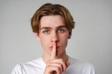 Young Man With Finger on Lips Signaling Silence Against a Plain Background