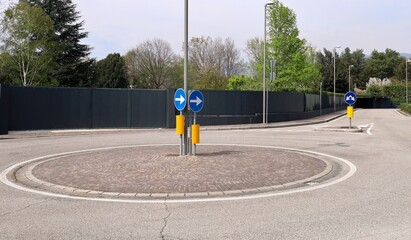 Roundabout with directional traffic arrow signs. Black anti noise panels on the left, empty road in...