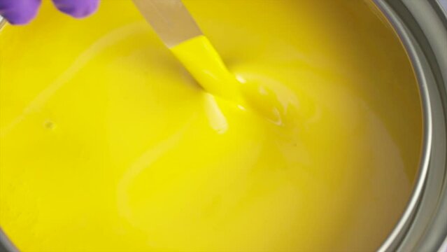painter dipping a spoon, stir paint into the bucket with yellow paint.