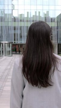 Vertical video. Back view of young adult business woman walking in a co-working office area. Professional confident empowered female entrepreneur going to work at the office.