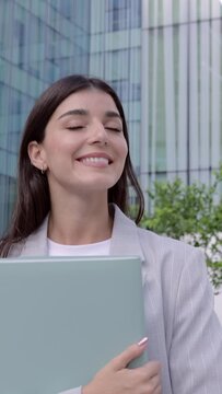 Vertical HD video. Cheerful young adult business woman walking outdoors corporate office buildings. Smiling professional empowered female entrepreneur going home after work day.