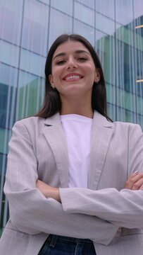 Vertical HD confidence portrait of young businesswoman with crossed arms standing over office building. Leadership, vision and empowerment concept. 9:16 screen video.