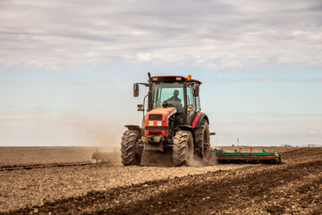 Fototapeta premium Powerful tractor at work, turning over soil on a vast farmland under a clear sky