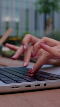 Vertical HD video. Close up of businesswoman hands typing on laptop keyboard sitting on outside bench at business office building. Freelancer people and business lifestyle concept.
