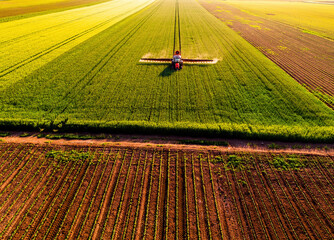 Aerial view of tractor spraying fertilizer on green field