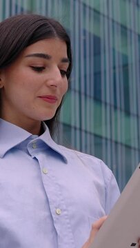 Vertical 9:16 portrait of a successful business woman using digital tablet over corporate modern business building. HD screen video.