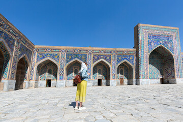 Happy attractive woman tourist in hat, posing at the entrance in Registan square Samarkand,...
