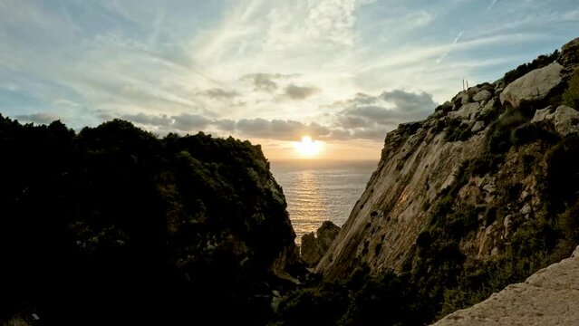 The sun sets over an enclosed bay, cliffs casting shadows in this captivating time-lapse