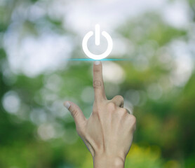 Hand pressing power button icon over blur green tree in park, Start up business concept