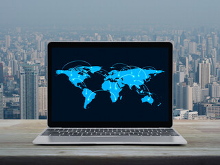Connection line with global world map on laptop computer monitor screen on wooden table over city tower and skyscraper, Business communication online concept, Elements of this image furnished by NASA - obrazy, fototapety, plakaty