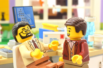 Fototapeta premium Boss and employee or two businessmen are discussing a problem or smiling in social media. A table with a computer in the office. Editorial illustrative image of lego.