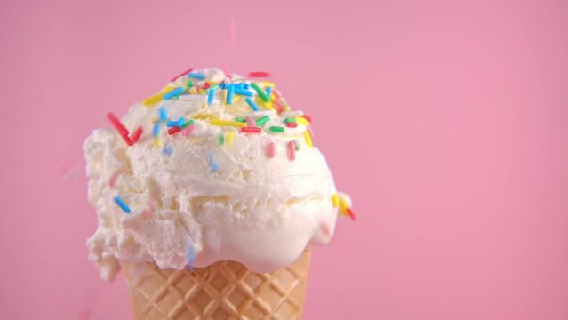 wafer cone with scoop of ice cream covered and strewing sprinkles on pink background, copy space, super slow motion, close up