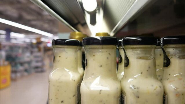 Close-up of many glass bottles of white sauce on a store shelf and a buyer's hand takes one