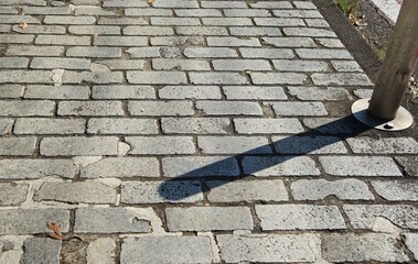 Cobblestone sidewalk on a sunny day and shade on a side pole