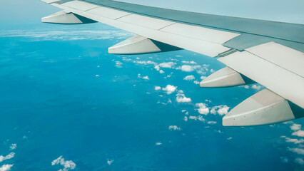Gazing from a plane's window, the view unfolds with a tranquil blue ocean below, dotted with clouds...