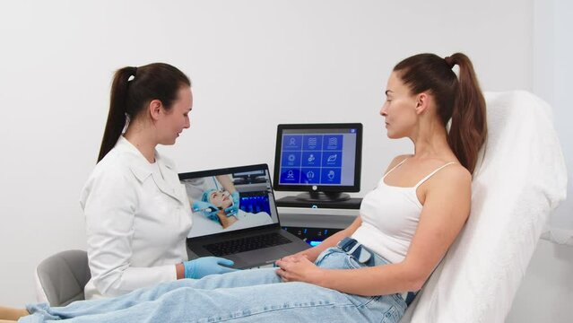 The cosmetologist shows the client a video of the hydrolifting procedure and conducts a consultation. A beautiful woman consults with a cosmetologist. Concept of anti-aging, cosmetology, beauty, facia