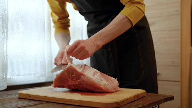 Unrecognizable man cuts off sinews from raw pork shoulder