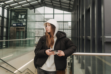 Tourist teenage girl at train station using smartphone map, social media check-in, or buy ticket booking. Modern travel app technology, lone traveler, Winter vacation railroad adventure concept