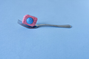 A fork with a dishwasher detergent tablet on a blue background, close-up