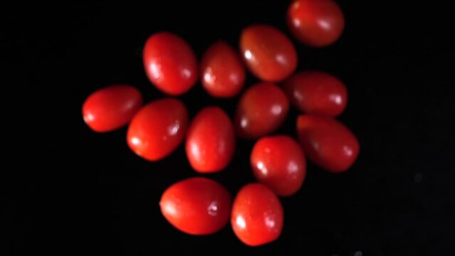 Small tomatoes fly into the air. Slow motion. Macro mode. Close-up. Black background