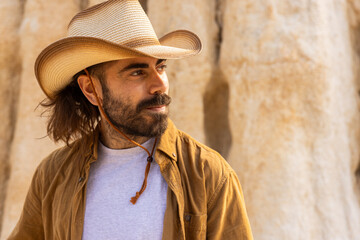 A man wearing a cowboy hat and a brown shirt is standing in front of a wall. He has a beard and a...