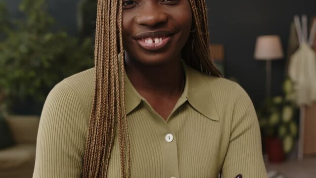 Tilt up slowmo portrait of young beautiful Black woman with lovely smile and long braided blond hair posing for camera with hands folded in contemporary green office