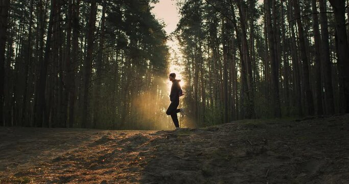 Wide shot of young man training in the forest. Outdoor rope skipping on sunrise. Silhouette of athlete with lens flair