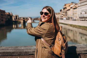 Photo sur Plexiglas Ponte Vecchio Stylish Happy Young woman in sunglasses enjoys beautiful view on famous Old bridge in Florence. Female traveler visiting Italian landmarks. Concept of travel, tourism and vacation in city