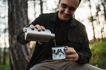One caucasian male pouring water in metal cup while hiking
