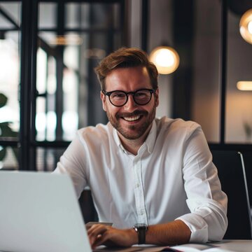 a confident and happy businessman sitting at a desk, focused on his work and using a laptop computer. he is appears to be in a comfortable work environment.