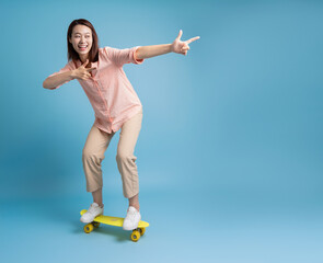 Photo of younf Asian woman skating on blue background