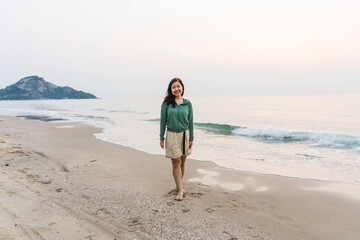 A woman walks along the sunny beach, enjoying the ocean waves - 782886205