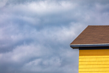 Yellow building and a dappled sky. Architectural detail of the traditional wooden houses of the Magdalen Islands, Canada. Space for text.